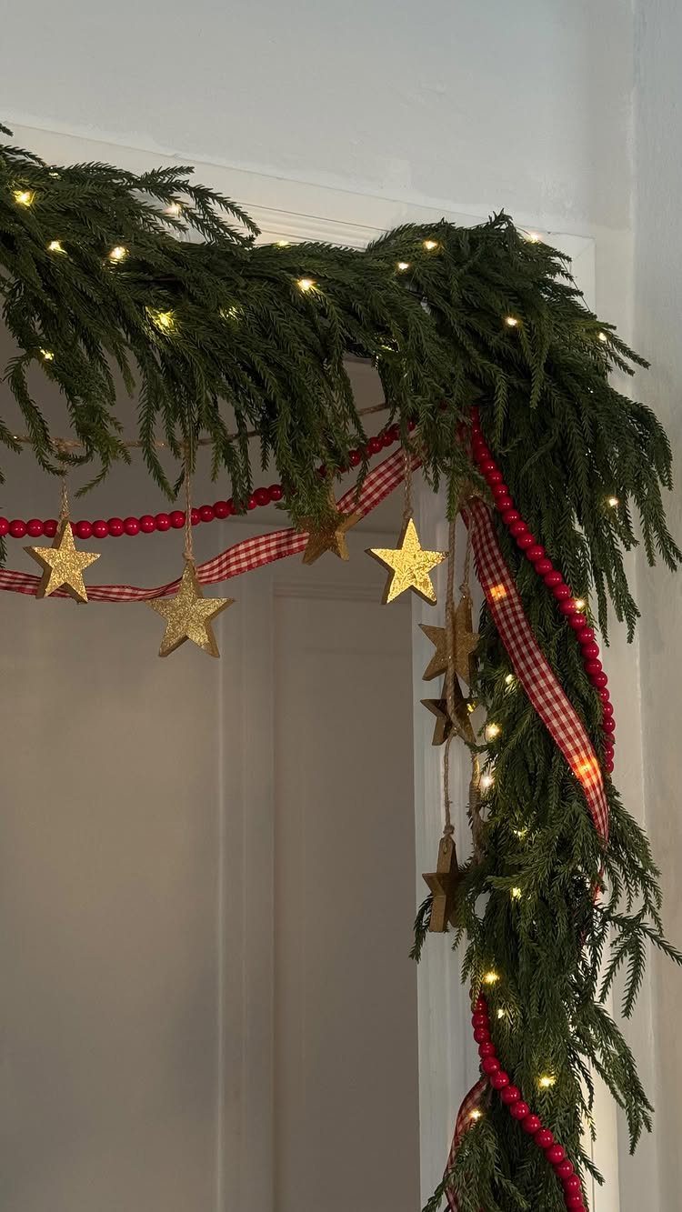 Green evergreen garland with fairy lights and gold stars draped over a doorway