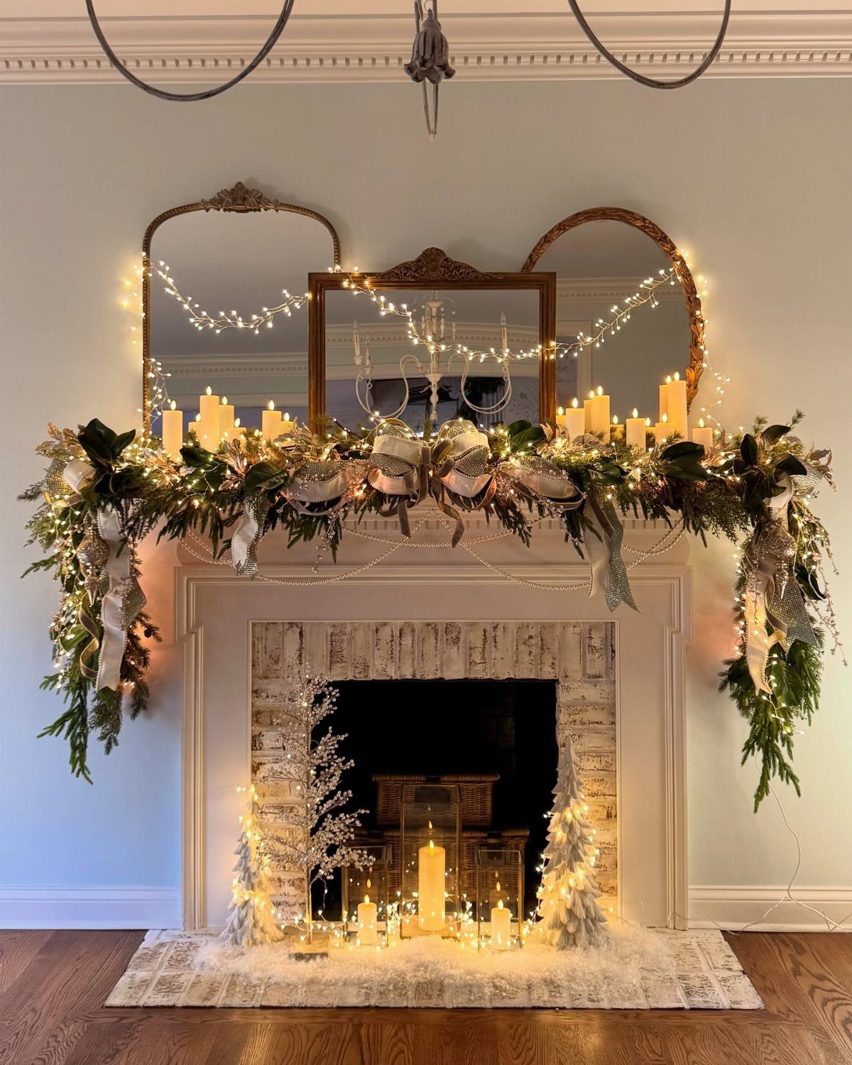 Decorated white fireplace mantel with green garlands, warm fairy lights, and white candles.