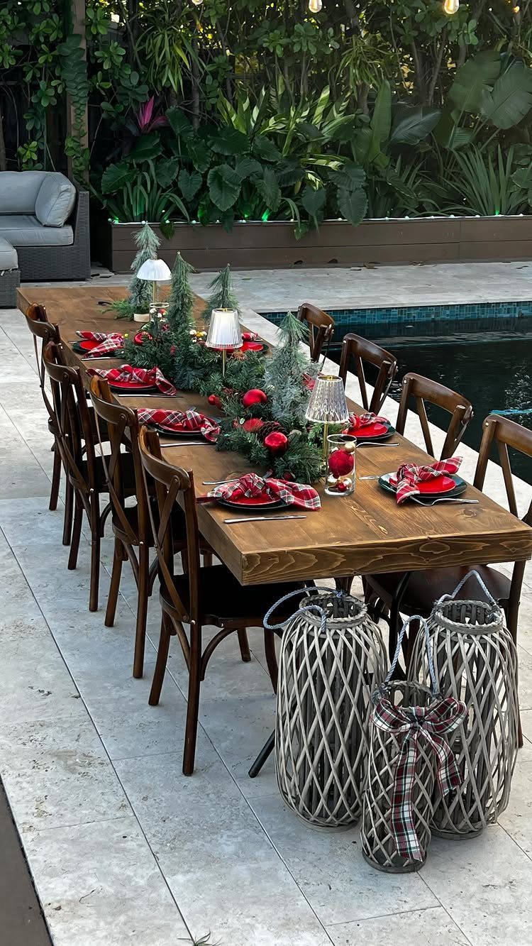 Wooden outdoor dining table decorated with Christmas greenery, red plaid napkins, and lanterns.