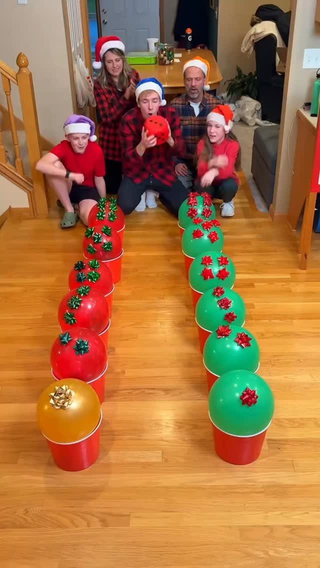 People in Santa hats playing a balloon game with red cups on wooden floor