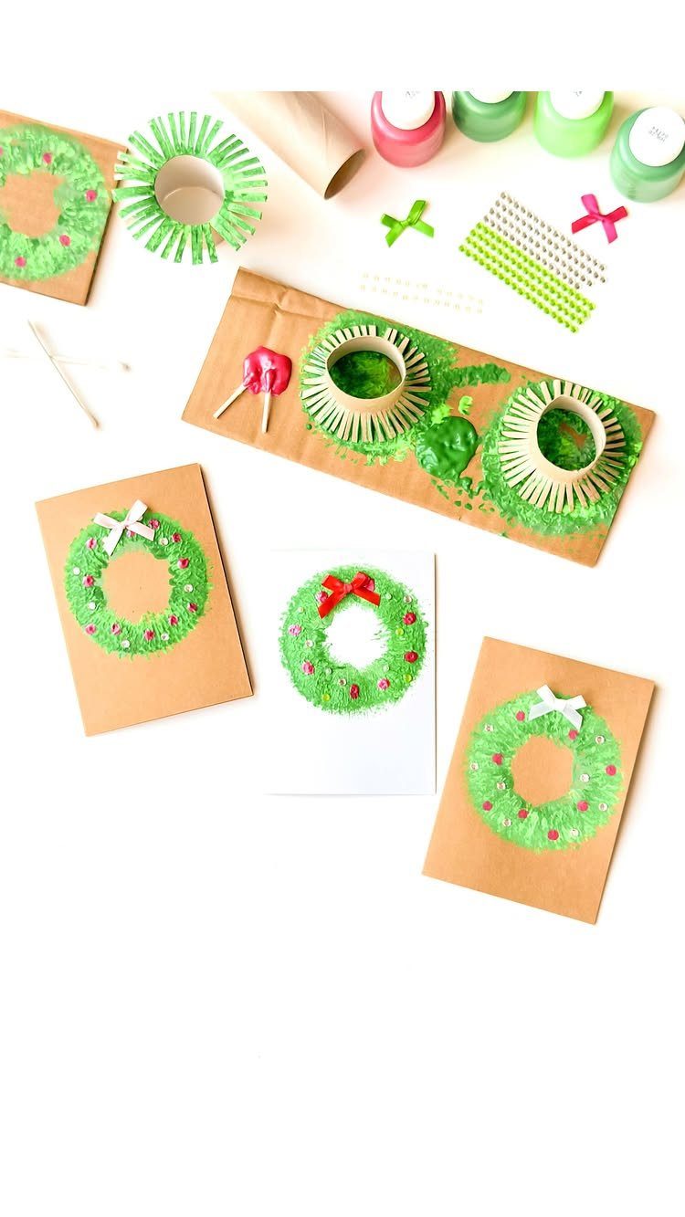 Handmade Christmas cards with green painted wreaths and small bows on a table.