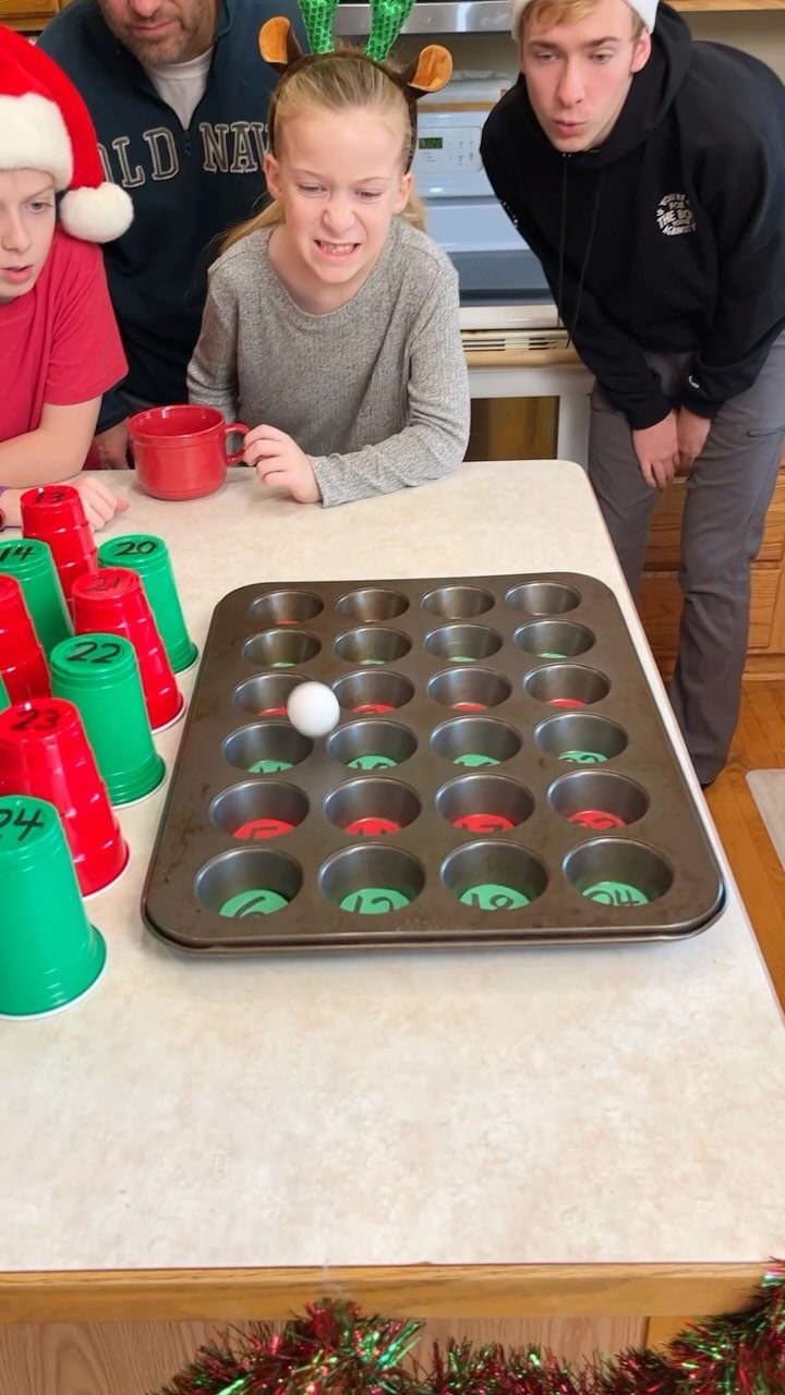 People playing a ping pong ball game with a muffin tin and cups.