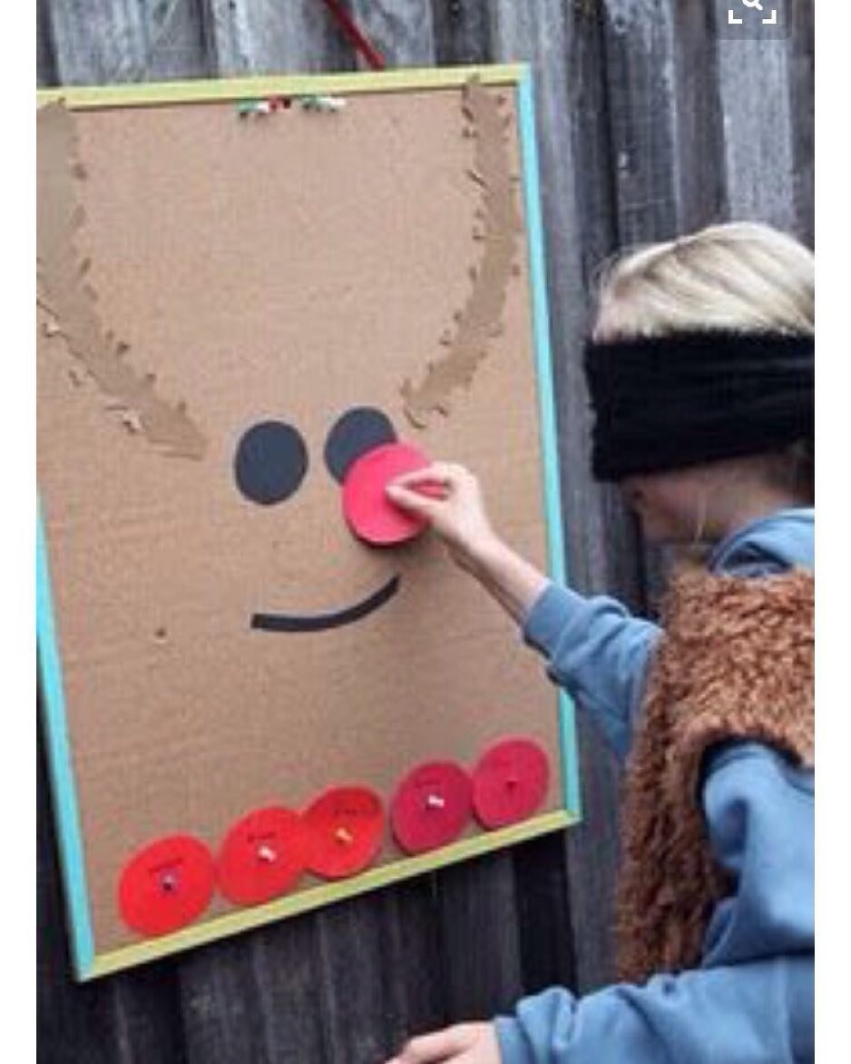 Blindfolded child placing a red nose on a cardboard reindeer game board.