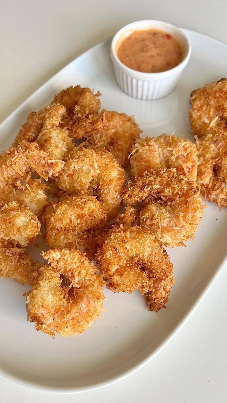 Coconut shrimp on a white platter with a side of orange dipping sauce.