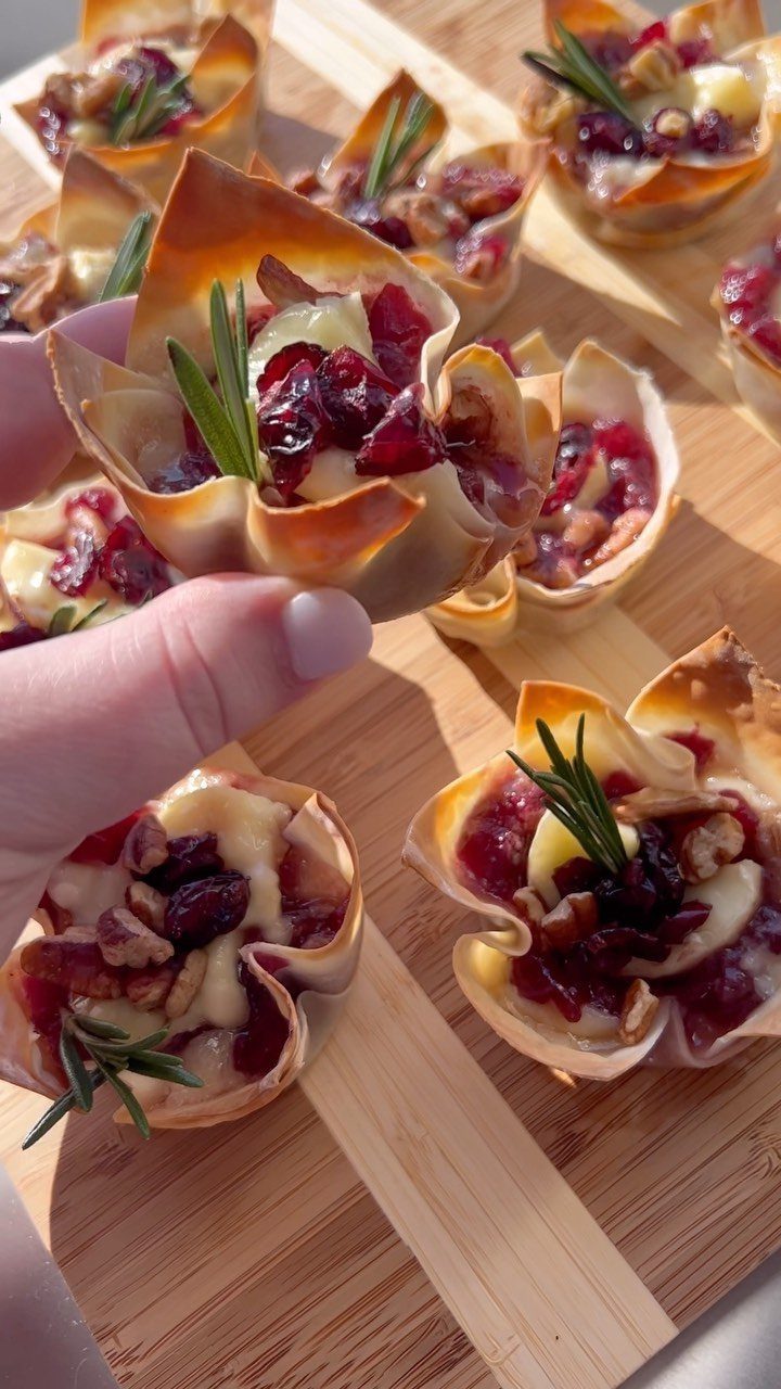 Brie bites with cranberry sauce and rosemary in phyllo cups on wooden board