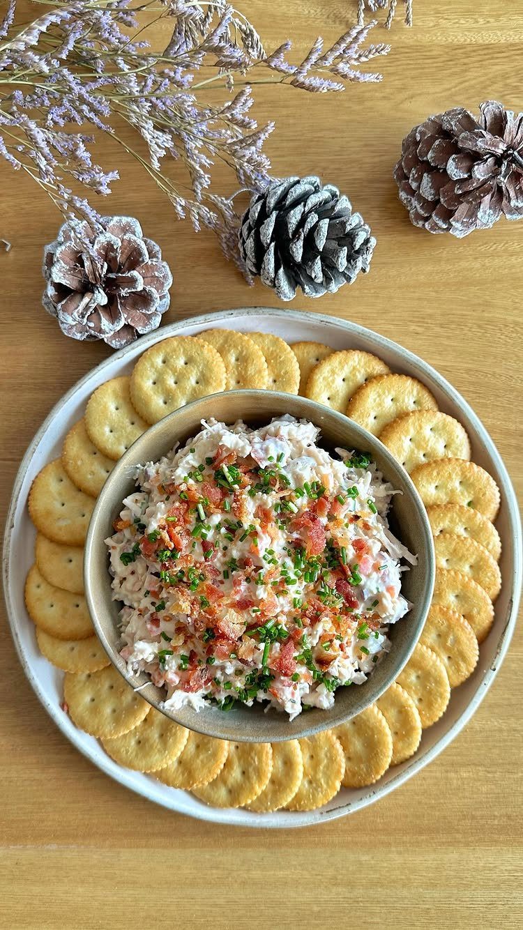 Creamy chicken dip topped with chives and peppers surrounded by round crackers.