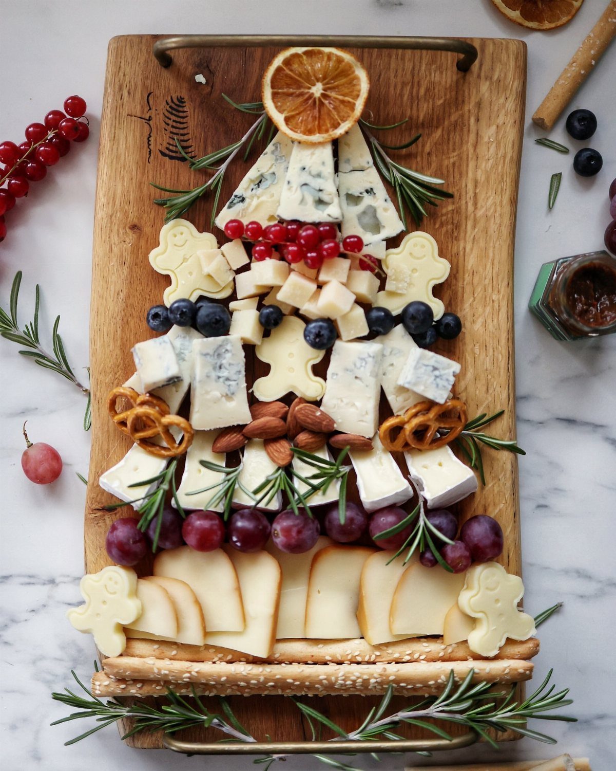 Christmas tree shaped charcuterie board with assorted cheeses, berries, nuts, and rosemary sprigs.