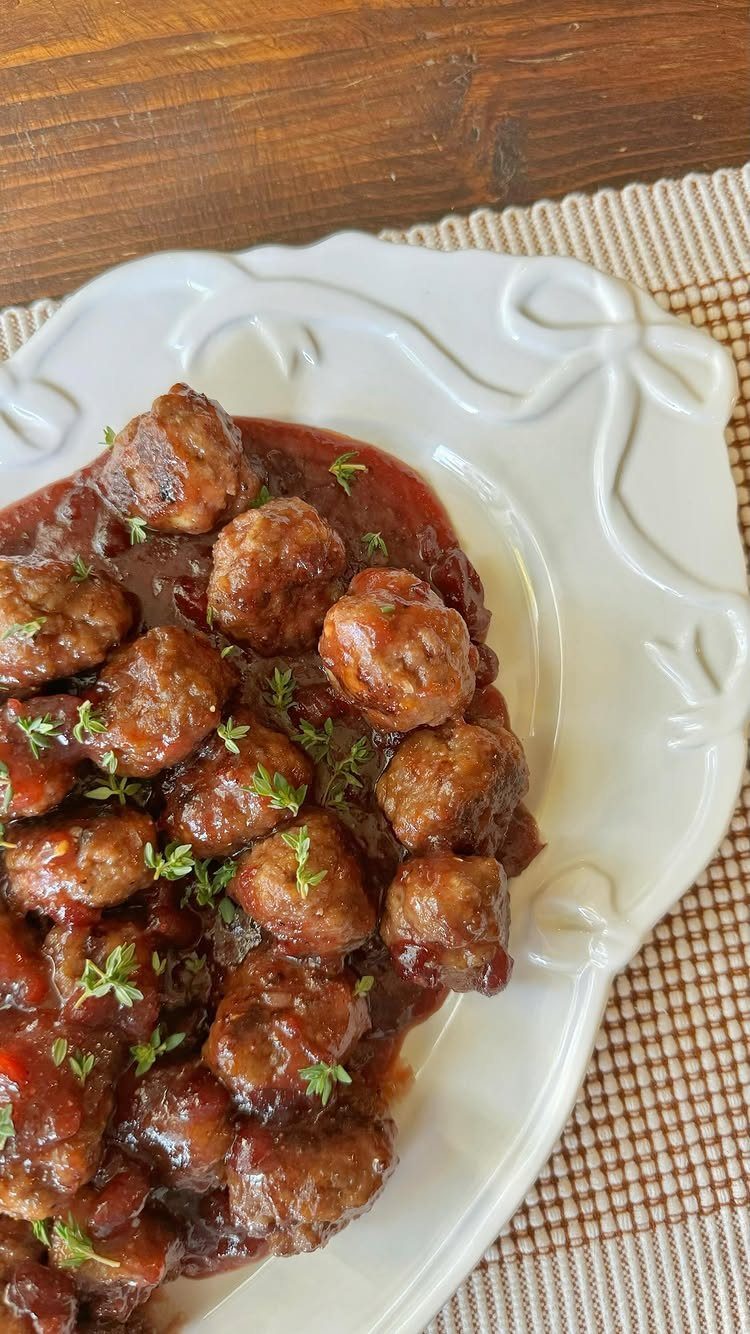Meatballs in a glossy red cranberry sauce garnished with fresh green herbs