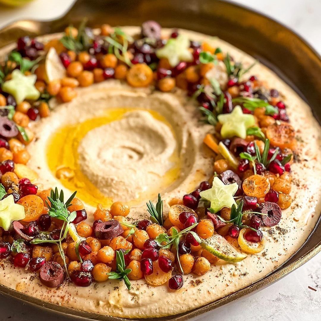Hummus platter decorated with a festive wreath of chickpeas, pomegranate, and herbs.