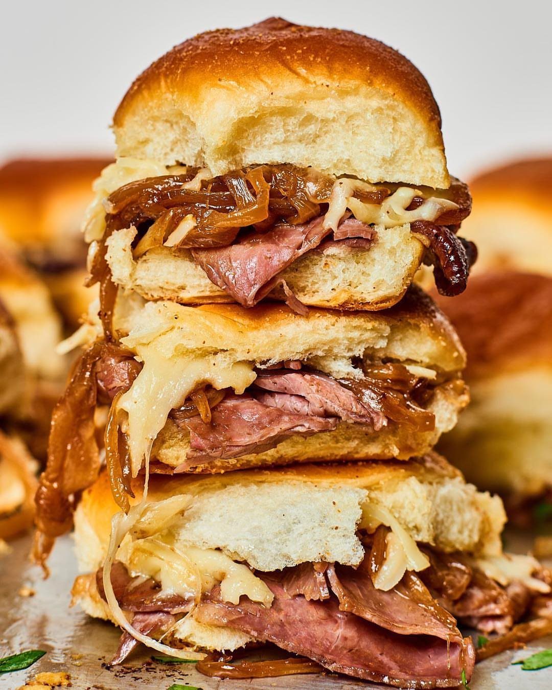 Three stacked beef sliders with melted cheese and caramelized onions on toasted buns.