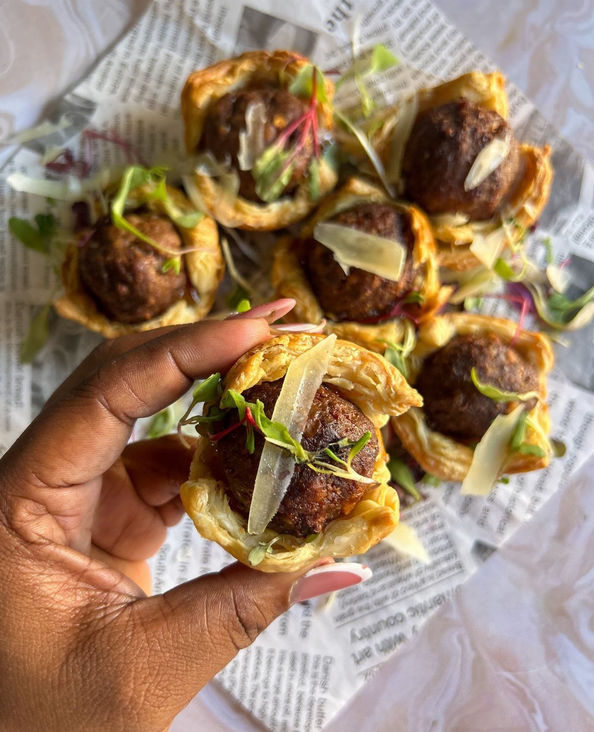 Meatball in a phyllo cup topped with cheese and greens held by hand