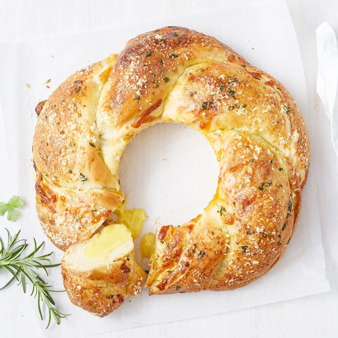 Golden-brown garlic bread wreath with melted cheese and herbs on white parchment paper.