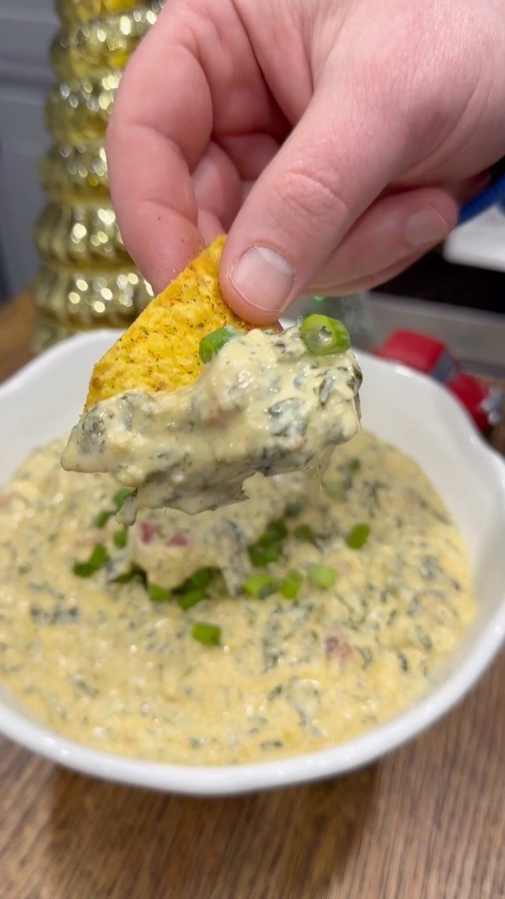 Tortilla chip dipping into creamy spinach and artichoke dip in a white bowl.