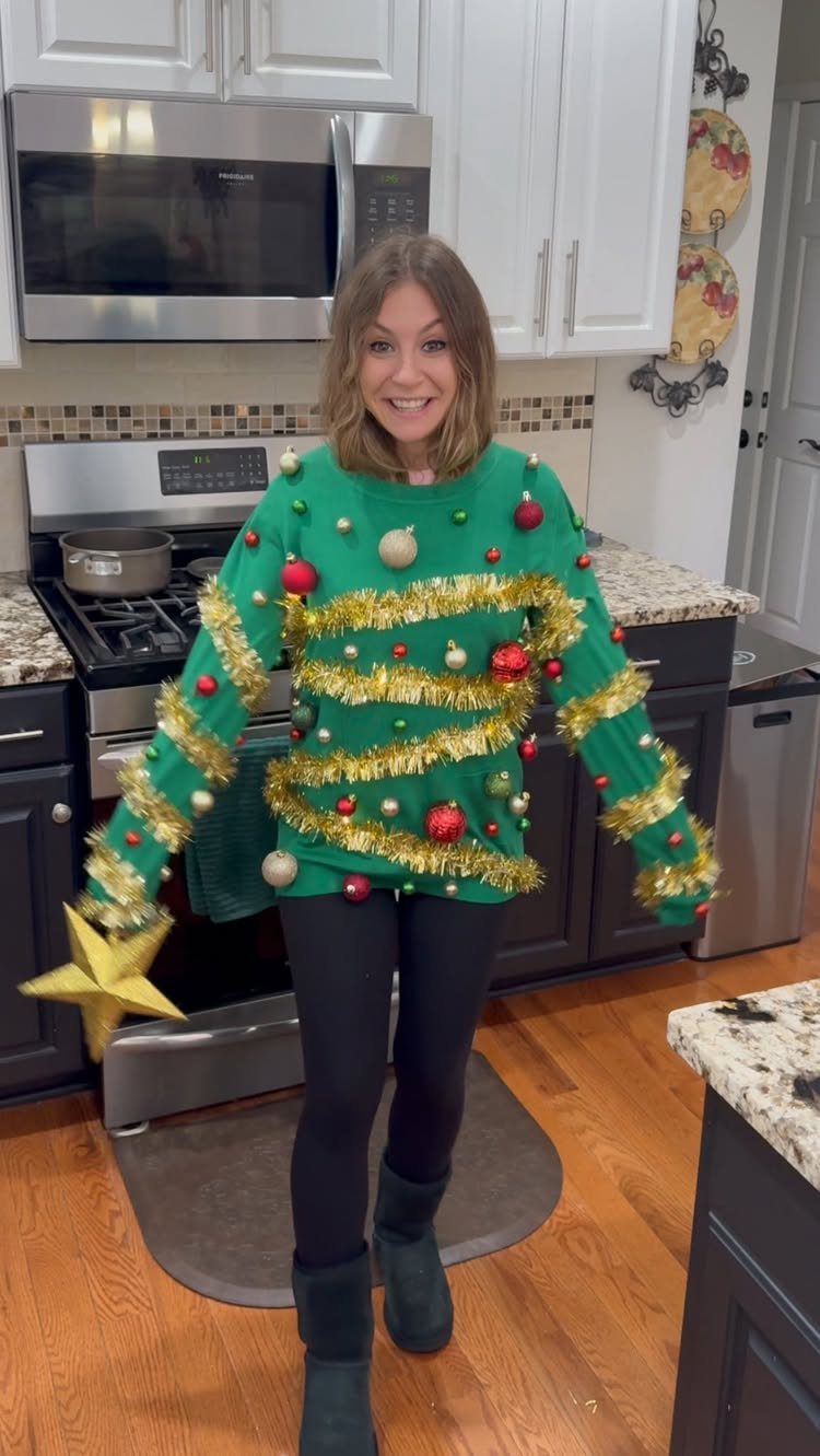 Woman wearing a green Christmas tree sweater with ornaments and tinsel in a kitchen