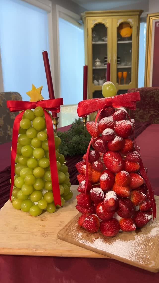 Fruit towers shaped like Christmas trees made from green grapes and strawberries with ribbons.