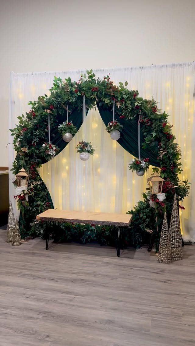 Circular greenery arch with red berries and fairy lights behind a wooden bench.