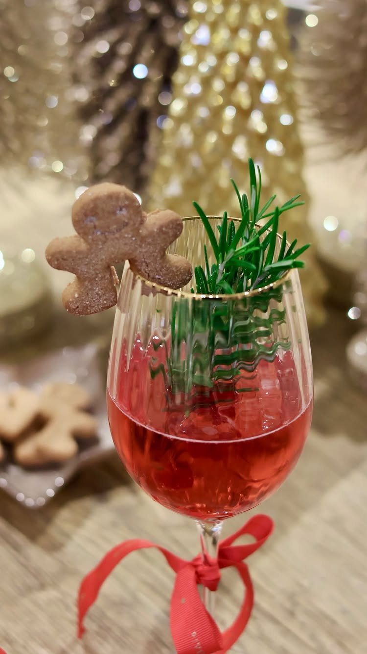 Red festive cocktail garnished with a gingerbread man and rosemary sprig