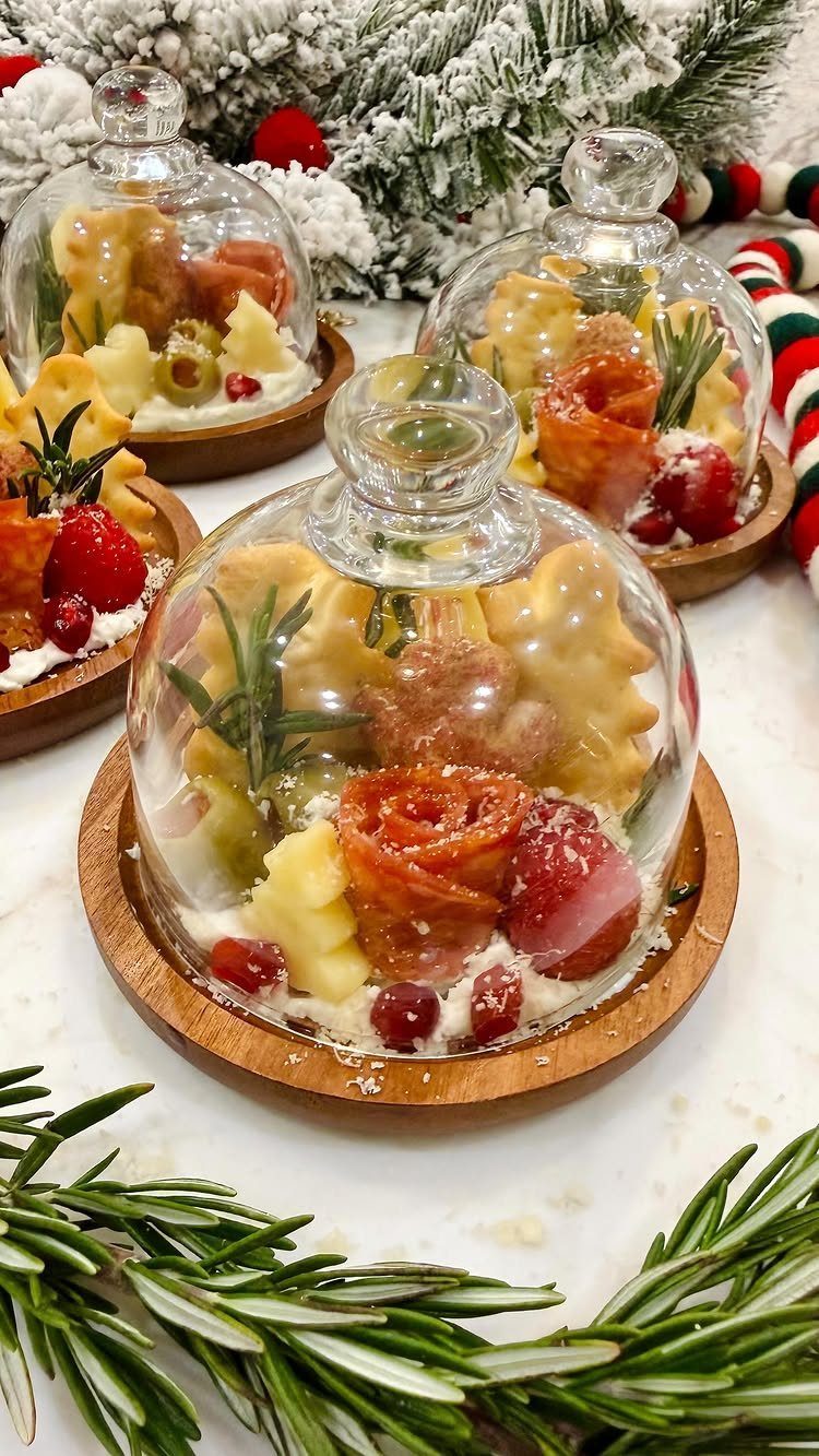 Festive cheese and charcuterie platters under glass cloches with snowy evergreen branches.