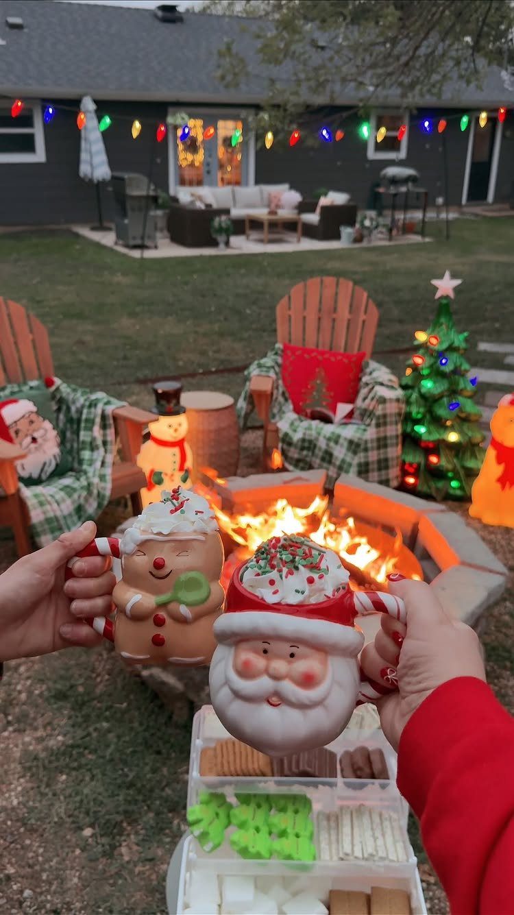 Festive Christmas mugs held over a fire pit in a decorated backyard setting.