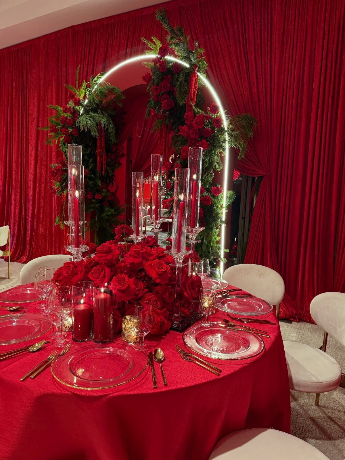 Red themed Christmas party table setting with roses, candles, and a glowing floral arch.