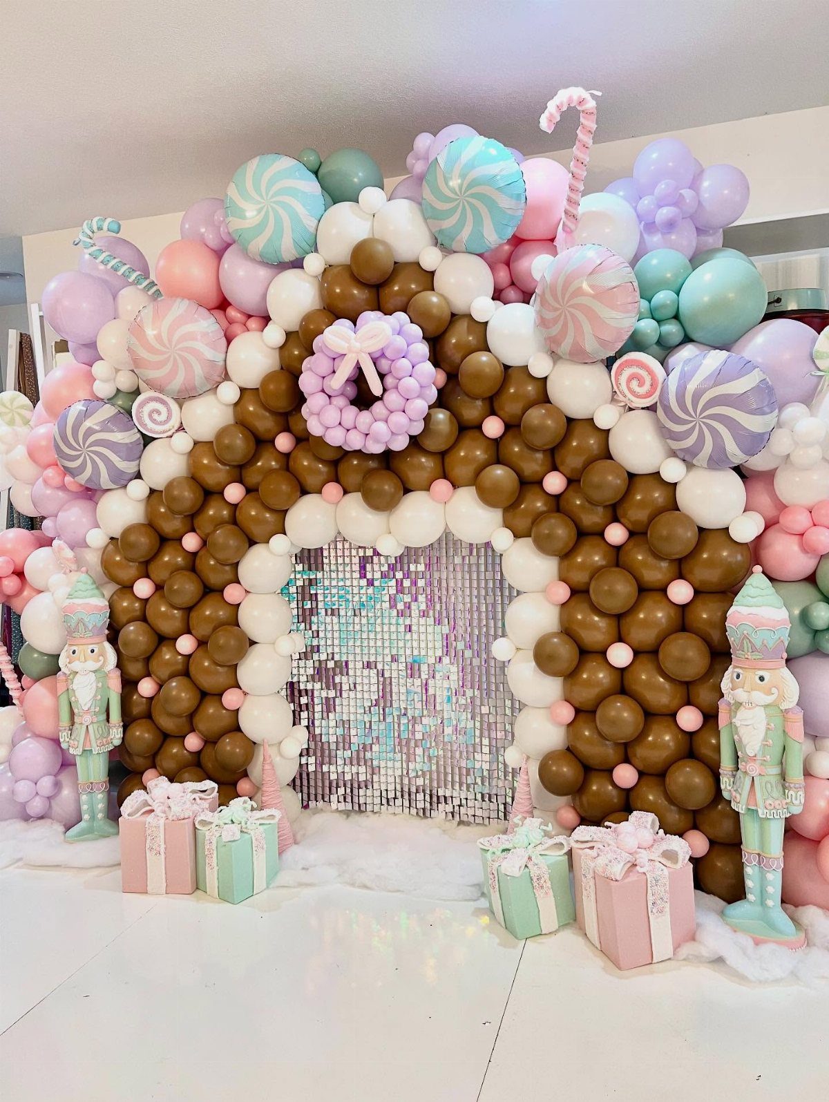 Candy-themed Christmas party balloon arch with nutcrackers and wrapped gift boxes.