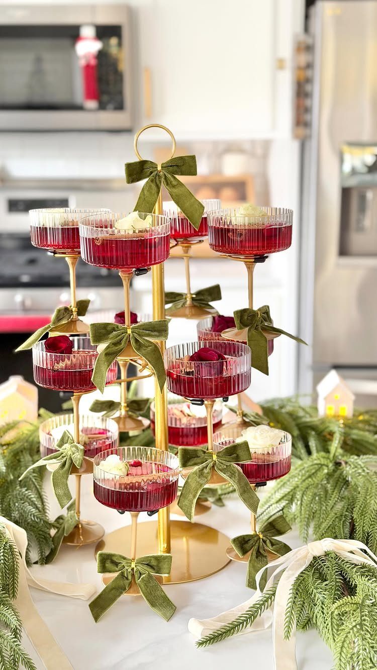 Red festive cocktails on a gold tiered stand decorated with green velvet bows.