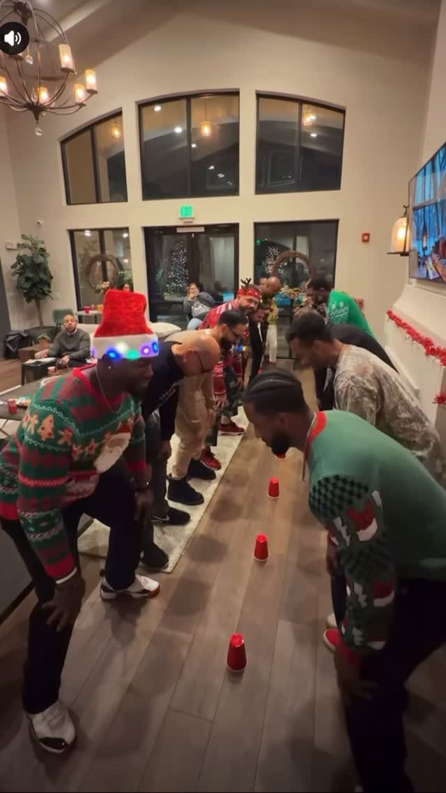 Men in Christmas sweaters playing a cup game on a living room floor.