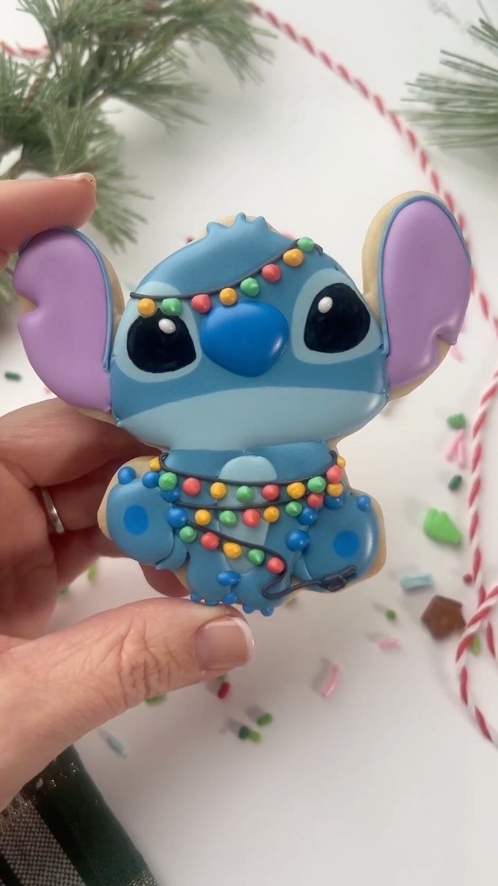 Stitch sugar cookie decorated with blue icing and colorful Christmas lights held by hand.