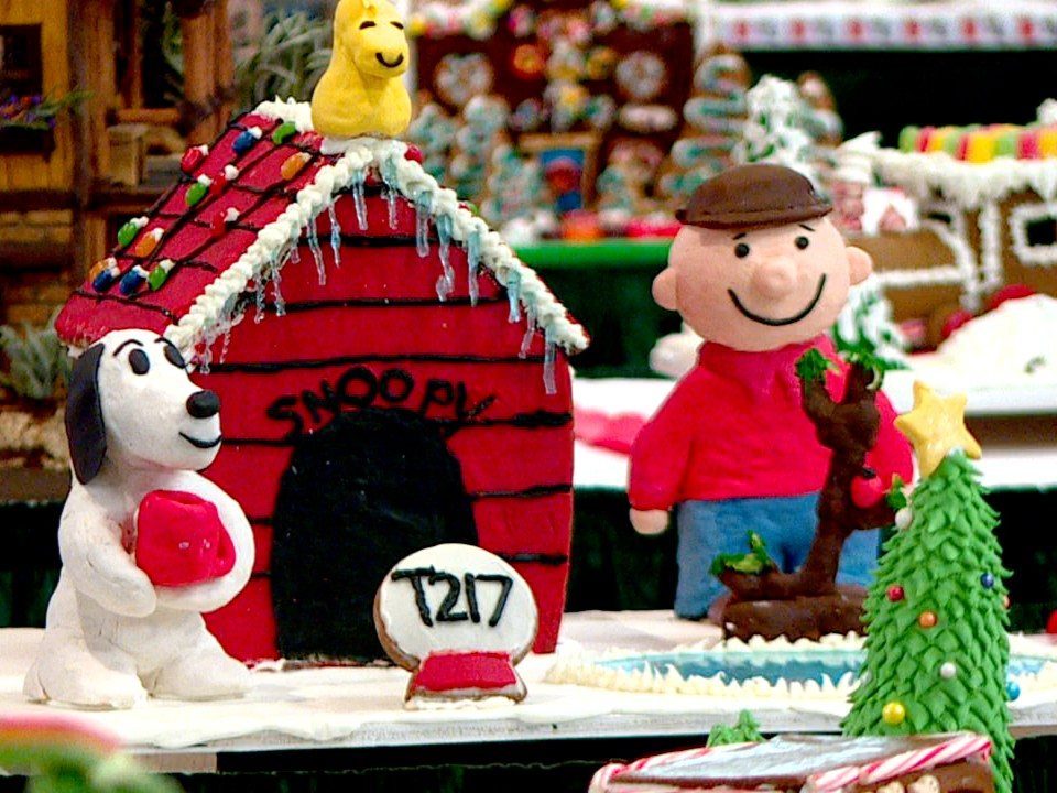 Gingerbread house shaped like Snoopy's doghouse with fondant Snoopy and Charlie Brown figures.