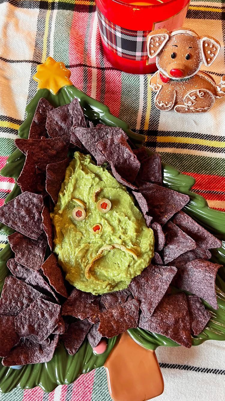 Guacamole shaped like the Grinch's face surrounded by purple chips on a tree platter.