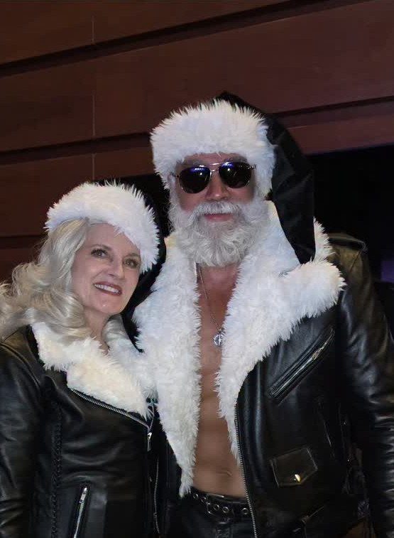 Man and woman in leather jackets and Santa hats posing for a photo.