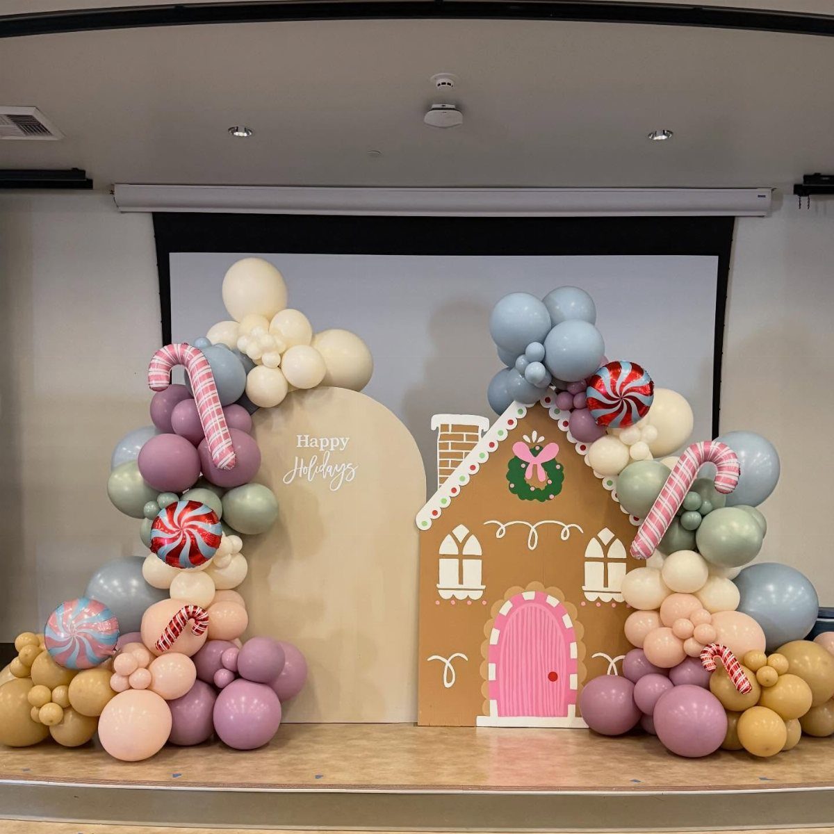 Gingerbread house party backdrop with pastel balloons and large candy cane decorations.