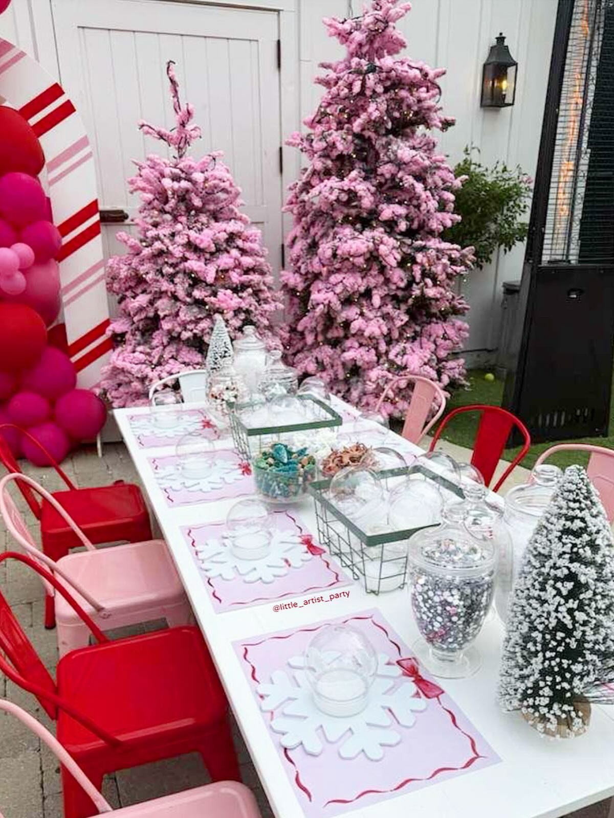 Pink and red Christmas party table setting with pink trees and balloons outdoors.