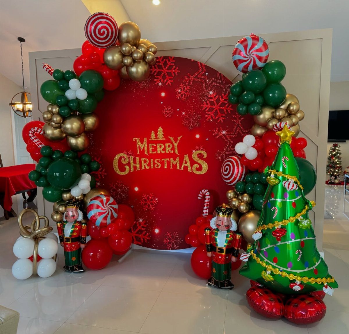 Christmas balloon arch with nutcrackers and a foil tree around a red backdrop.