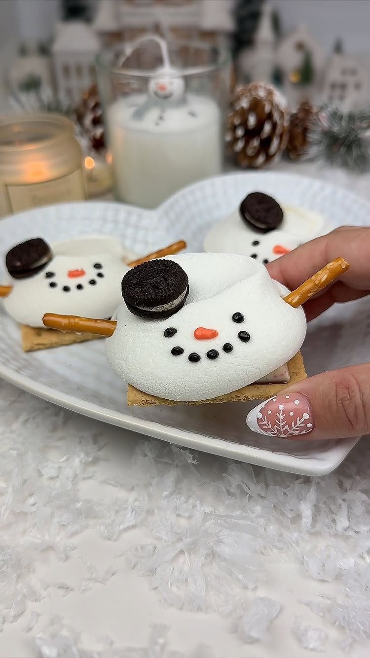 Snowman s'mores with marshmallow bodies and cookie hats on a white plate.