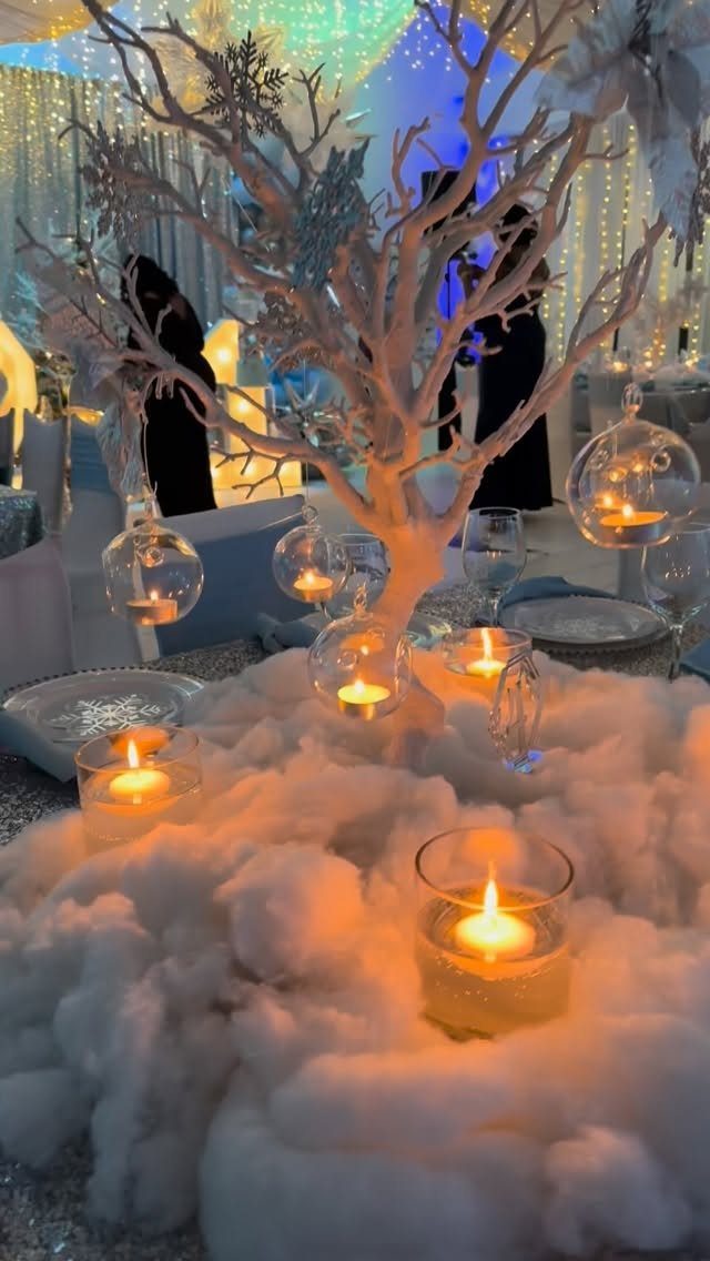 White decorative tree with glowing candles set in fluffy white faux snow.