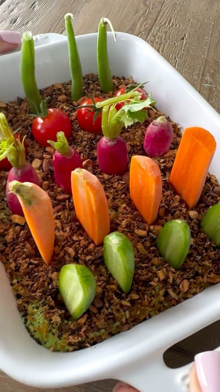 Vegetable arrangement with carrots, radishes, and peas on a textured brown base.