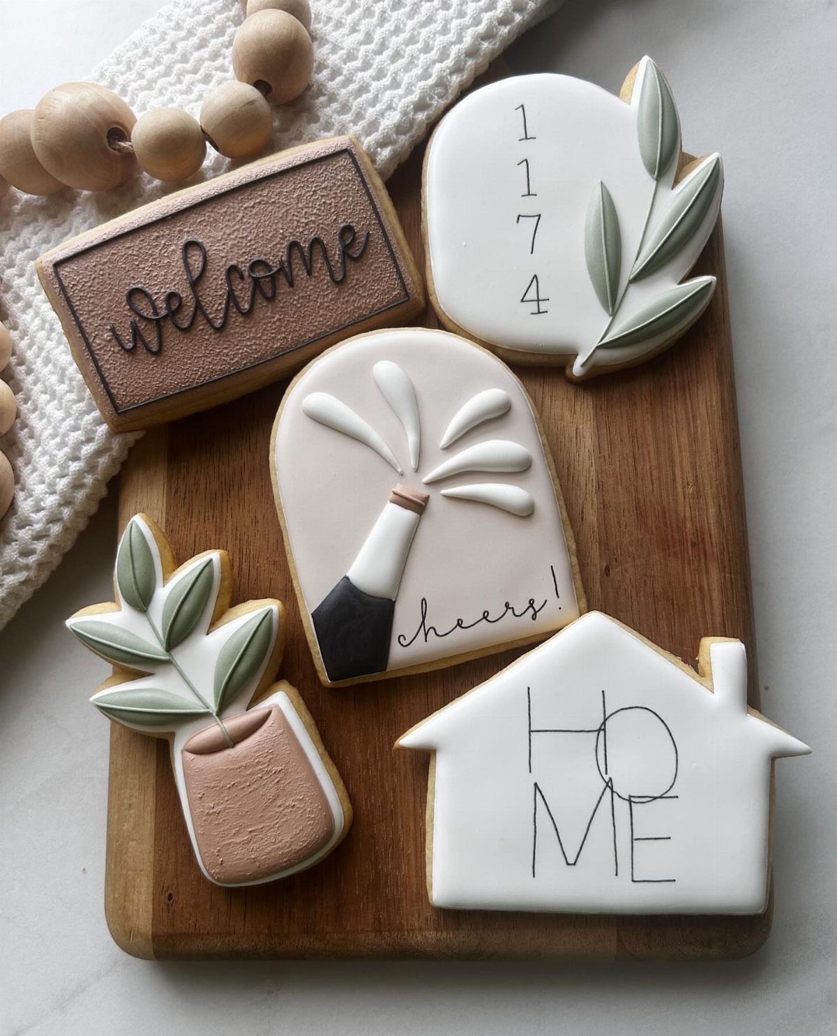 Iced sugar cookies shaped like a house and champagne bottle on a wooden board.