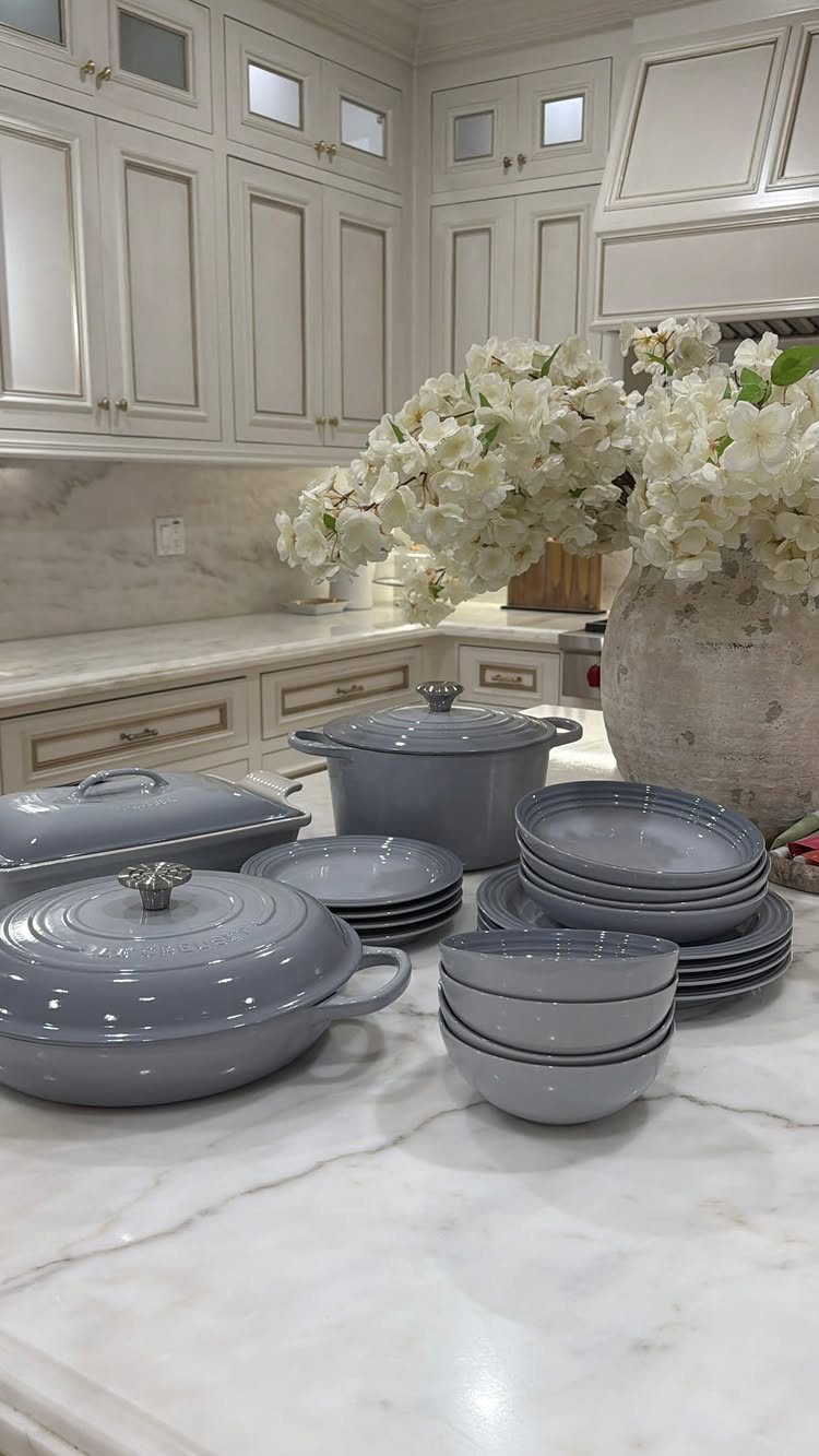 Grey ceramic cookware set and white flowers on a white marble kitchen counter