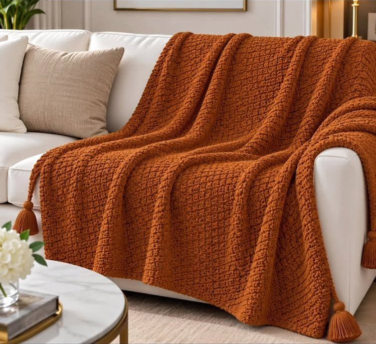 Burnt orange knit throw blanket with tassels draped over a white living room sofa