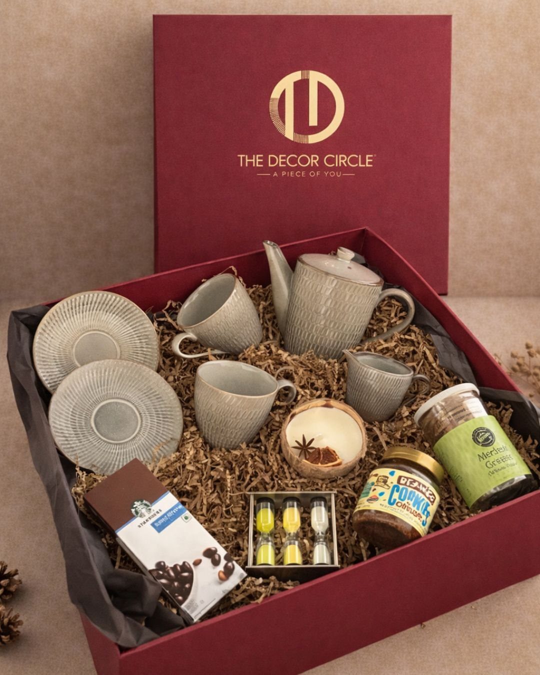 Red gift box containing a grey ceramic tea set and gourmet food treats.