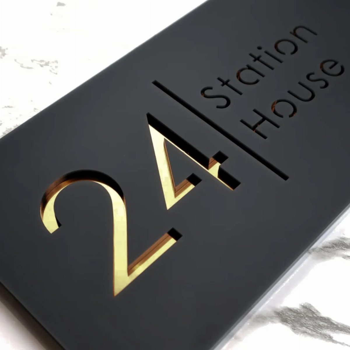 Black house sign with gold number 24 and Station House text on marble.