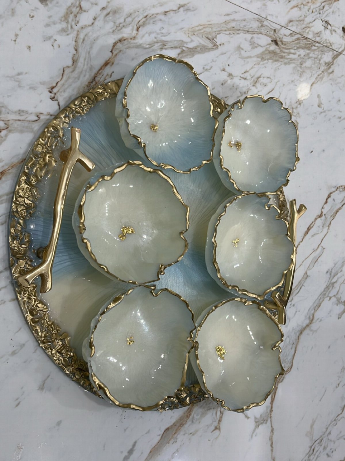 Six iridescent white and blue decorative bowls on a gold-rimmed tray over marble.