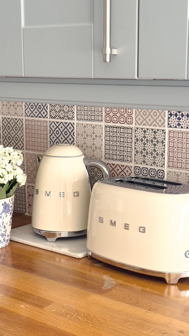 Cream Smeg electric kettle and toaster on a wooden counter with patterned tiles.