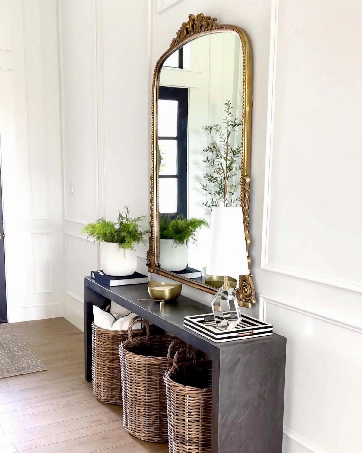 Dark grey console table with gold mirror, white lamp, and woven wicker baskets.