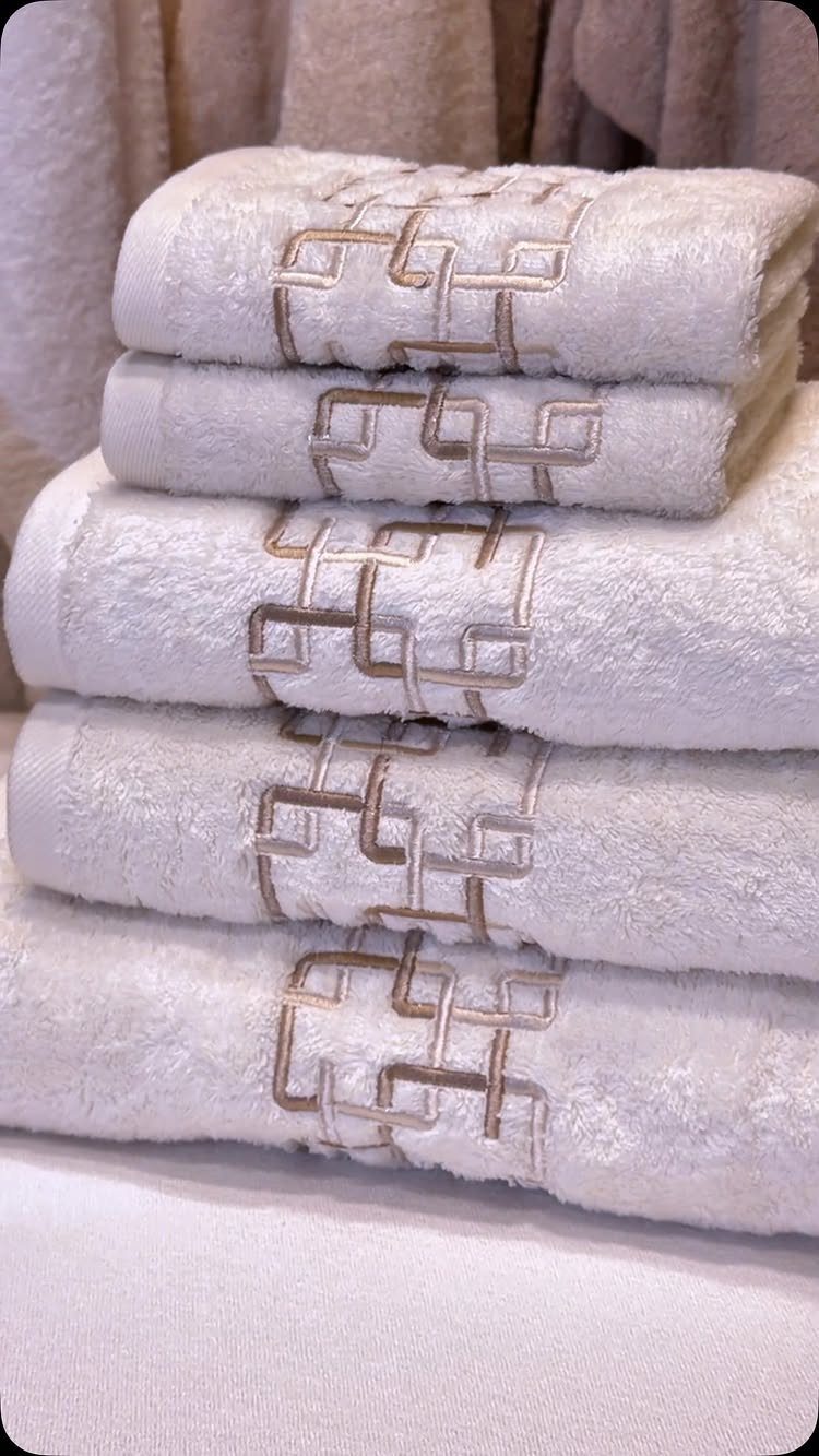 Stacked white plush towels with brown geometric embroidery on a white background