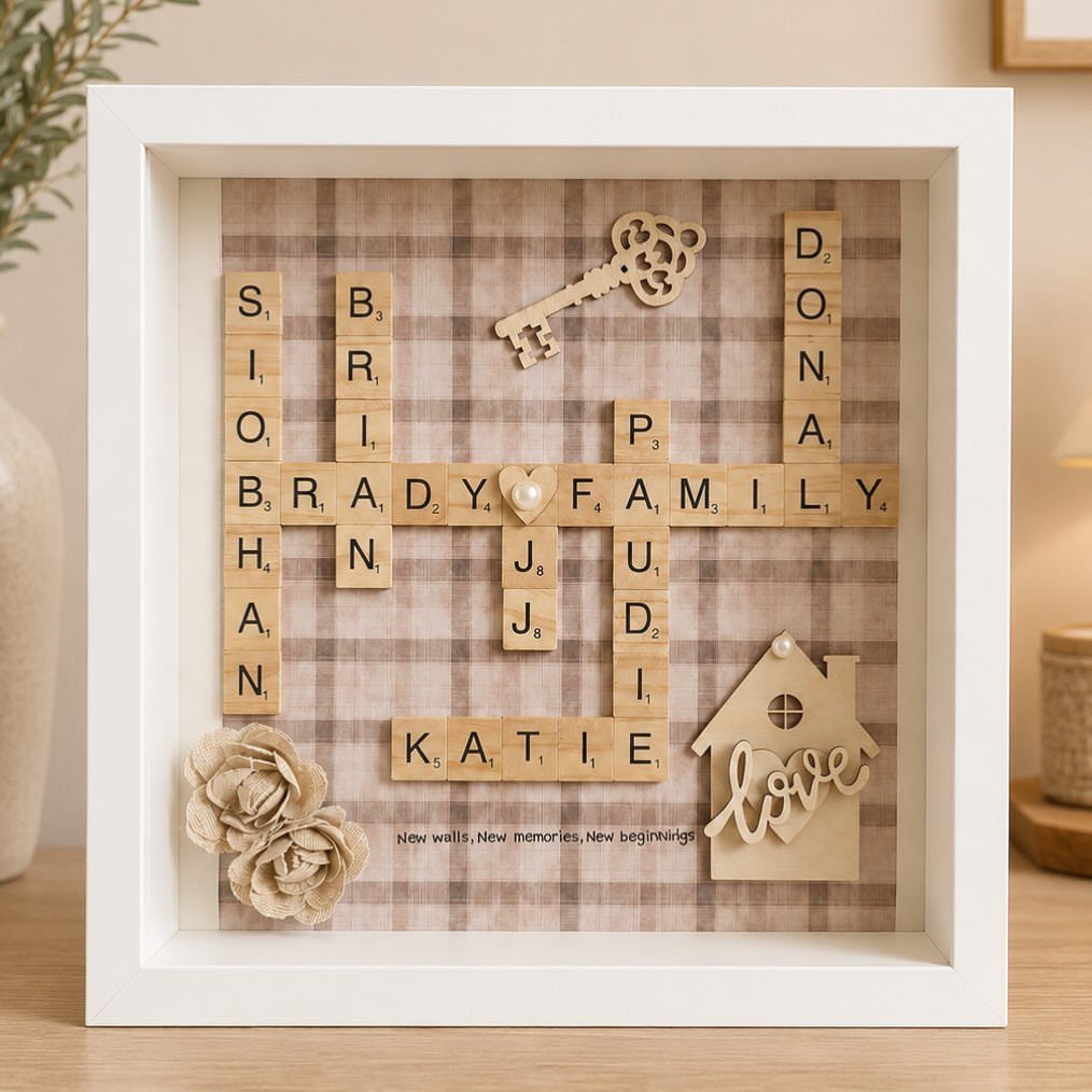 White shadow box frame with wooden letter tiles spelling family names and a house.