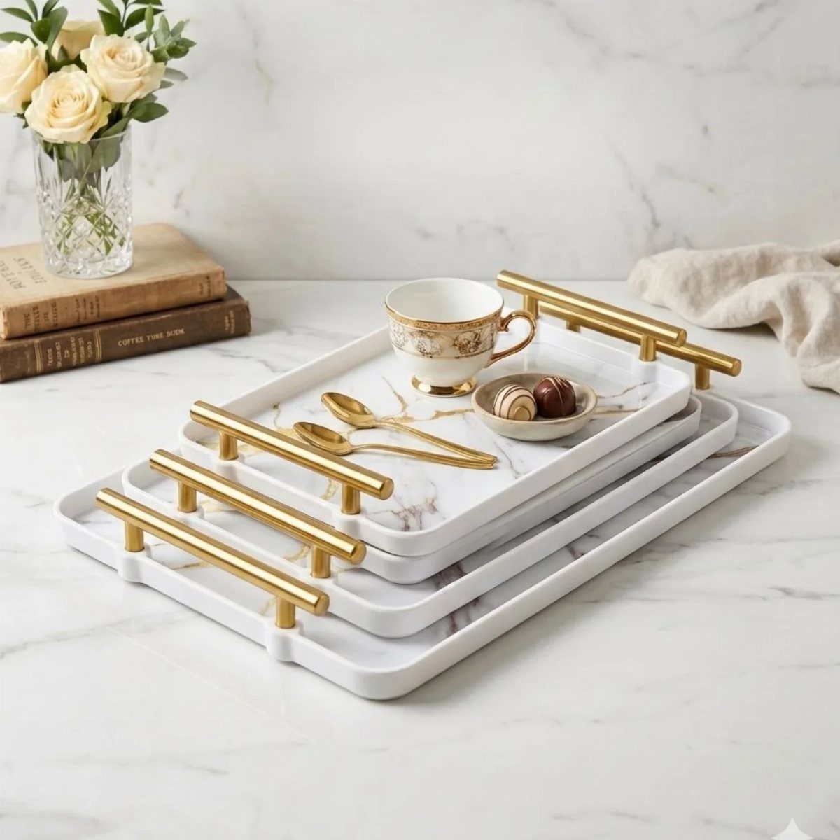 Three nested white marble serving trays with gold handles holding tea and chocolates.