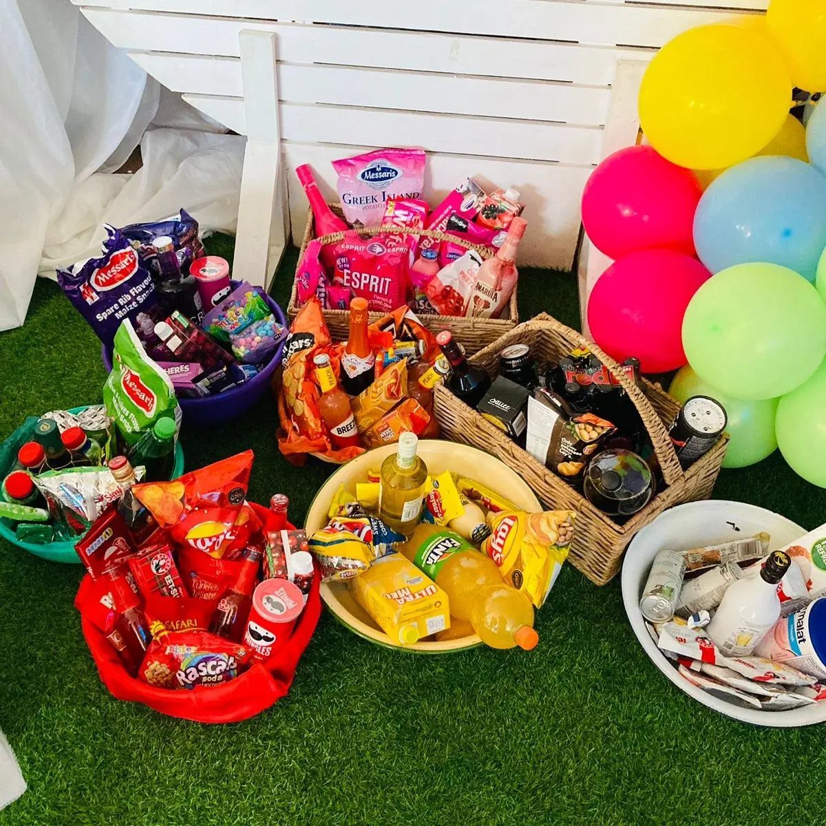 Color coordinated snacks and drinks in bowls next to bright colorful balloons.