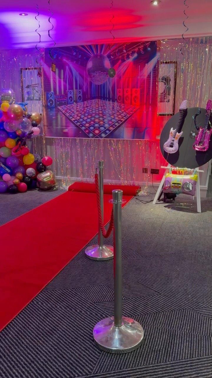 Red carpet entrance with disco backdrop, colorful balloons, and pink party lighting.